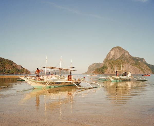 A photograph from the book shows fishing boats in what appears to be the middle of the day, with the sun high, their boat anchored between two mountains in the distance.